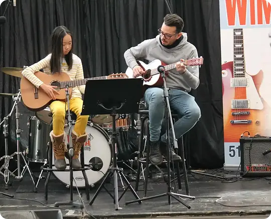 Guitar instructor and student performing together on stage